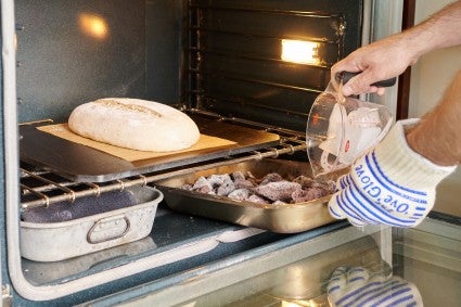 Adding water to roasting pan fill of lava rocks to bake bread