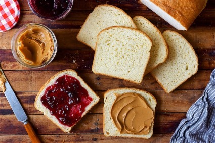 Loaf of white sandwich bread sliced on a table, two slices spread with peanut butter and jelly