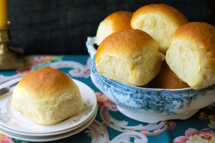 Amish Dinner Rolls, one on a plate, more in a pretty stoneware bowl behind