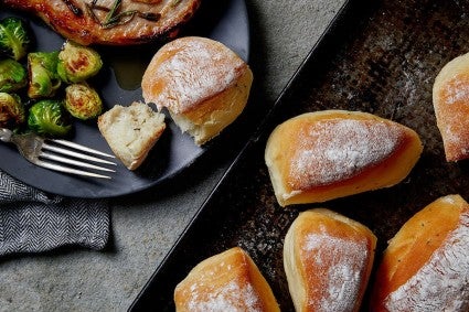 Flour-dusted rosemary potato rolls on a tray set on a table.