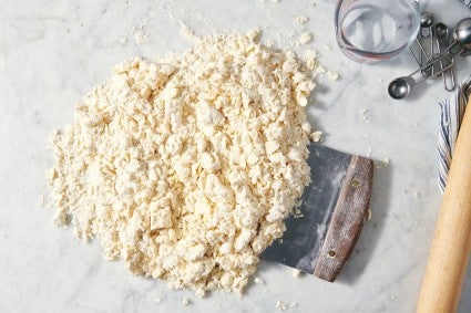 Pie dough being cut and mixed with a bench knife on work surface