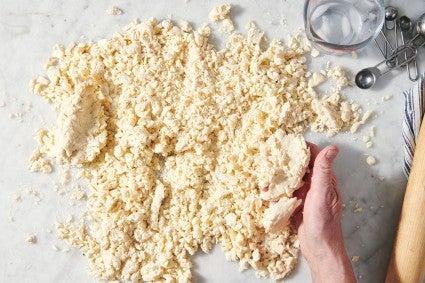 Pie dough being squeezed to form large clumps on work surface