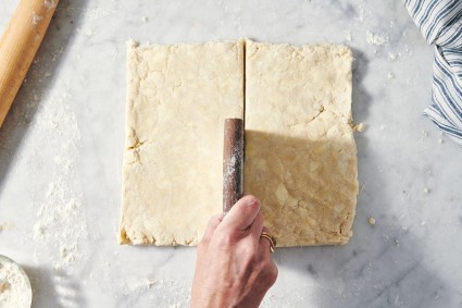 Square of pie dough cut in half with bench knife