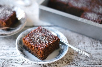 Piece of gingerbread on plate dusted with powdered sugar. 