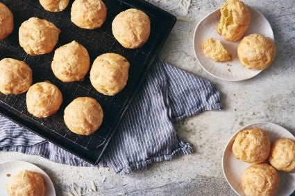 Batch of baked gougères in pan, and plates of more gougères. 