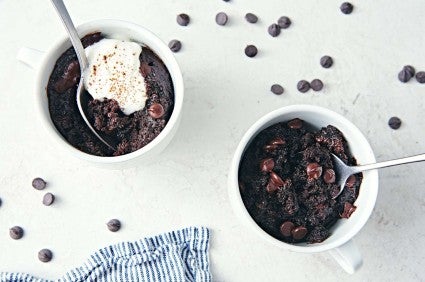 Two cups of chocolate-mug cake with chocolate chips sprinkled on the table nearby. 