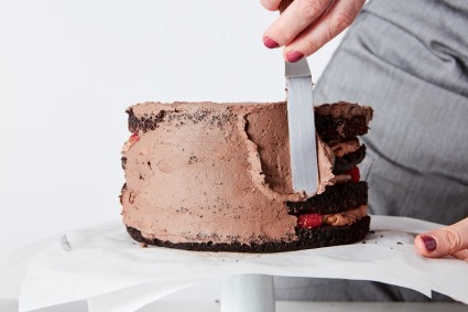 Baker using offset spatula to frost sides of a chocolate cake