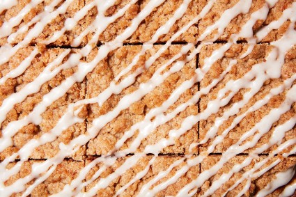 A close up shot of the crumb topping of slices of coffee cake drizzled with glaze