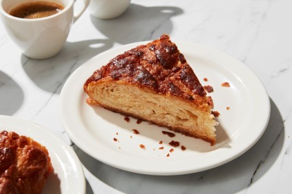 One slice of Kouign-amann on a plate with a cup of coffee nearby. 