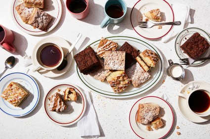 A diner scene with lots of different kinds of coffee cake with coffee cups