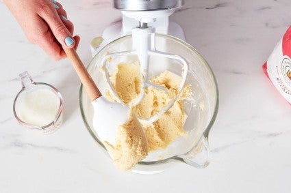 A baker holding up a mixture of butter creamed with the dry ingredients of the cake on a spatula