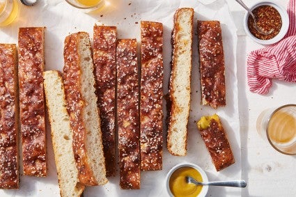 A pretzel focaccia cut into long strips on a cutting board next to an assortment of dipping sauces