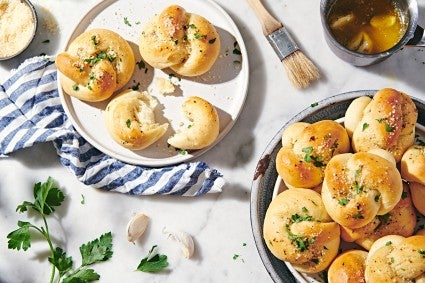 A platter of soft garlic knots on a table with some torn in half to show the soft interior