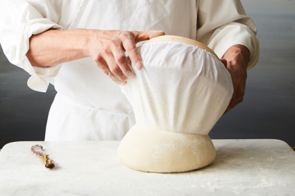 Baker removing cloth lined banneton from upturned bread dough 