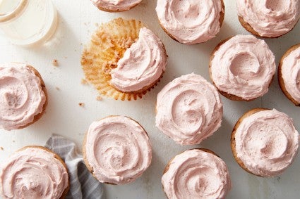 Overhead shot of frosted cherry cupcakes and a glass of milk. 