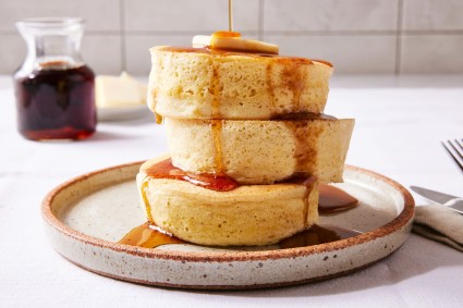 Stack of three fluffy pancakes with syrup on a plate.