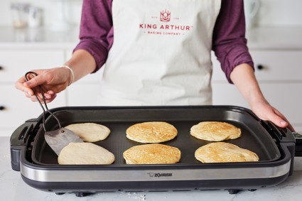 Baker cooking a batch of six pancakes on an electric griddle