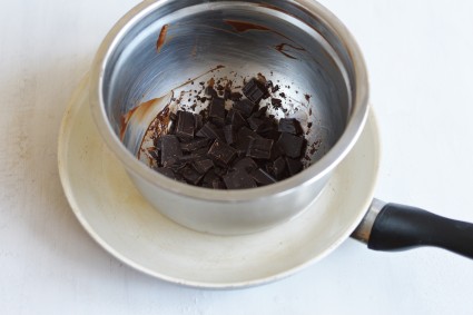 Chopped chocolate in metal bowl set in skillet full of water