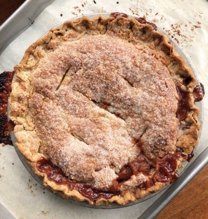 Apple pie with perfectly browned top crust and edge, bubbling filling leaking out of the side,