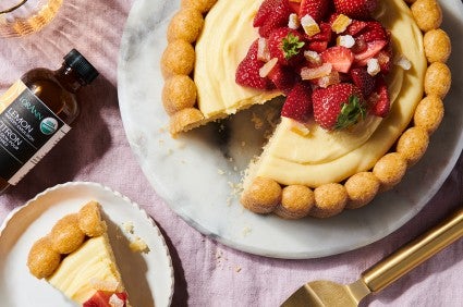 A lemon cake bakd in a Charlotte pan and filled with lemon pastry cream next to a bottle of lemon emulsion