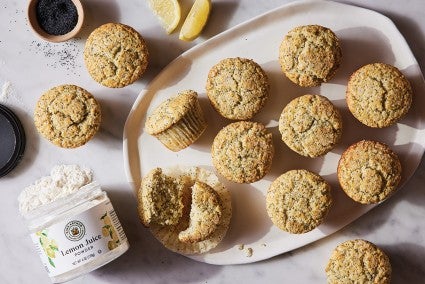 A platter of lemon poppy seeds muffins next to an open jar of lemon juice powder