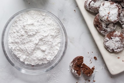 Bowl of confectioners' sugar next to chocolate cookies covered in confectioners' sugar