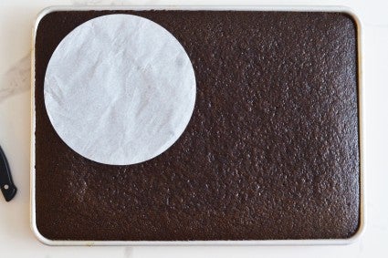 Chocolate cake in half-sheet pan, with a 8" round parchment to cut out