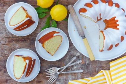 A lemon Bundt cake covered with glaze with a few slices on plates next to it