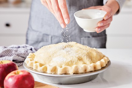 Baker sprinkling the top of an unbaked apple pie with sparkling sugar