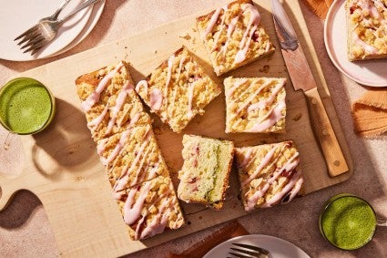 A strawberry coffee cake with matcha filling cut into slices, surrounded by cups of matcha (green tea)