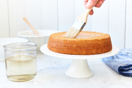 Baker using pastry brush to brush simple syrup onto a round cake layer