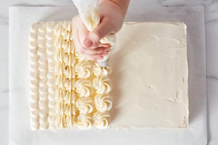 Baker piping frosting onto a sheet cake with star tip