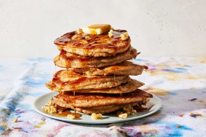 Stack of banana pancakes with syrup and butter dripping down sides.