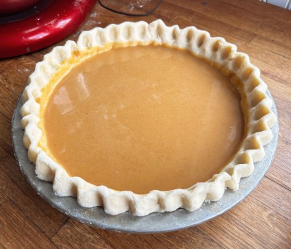 Pumpkin pie custard poured into a crimped pie shell in a pan, ready to bake.