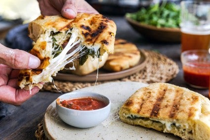 Hands holding and pulling apart calzone showing melted cheese and fillings inside.