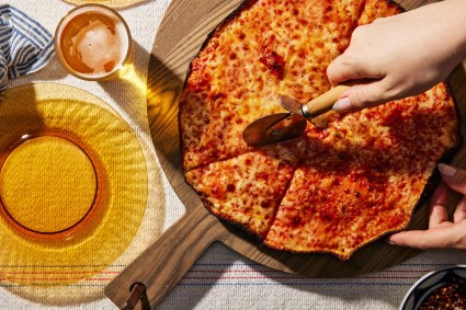 Overhead shot of hand using a pizza cutter to slice the pizza. 