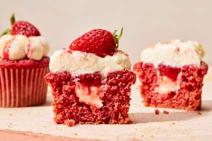 Bright red cupcakes cut in half with cream cheese and strawberry filling showing.