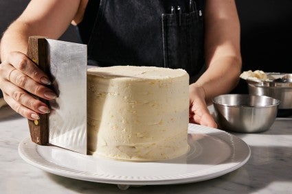 White icing being smooth onto a cake with a bench knife and microwave DIY turntable