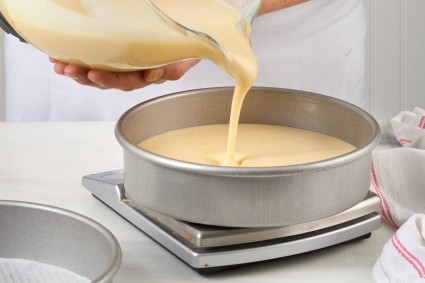 Baker pouring cake batter into round cake pan