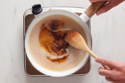 Baker using wooden spoon to stir brown butter on the stovetop