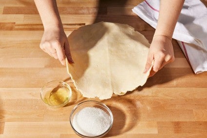 A baker placing pie dough over the top of an apple pie