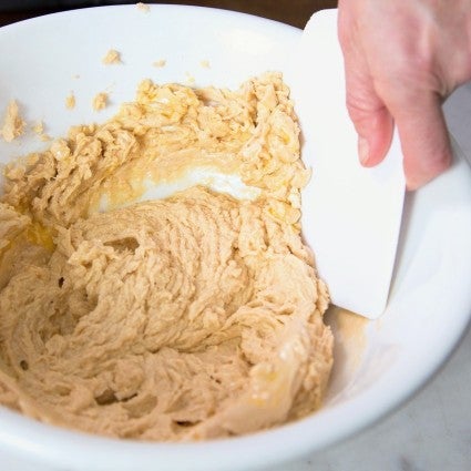 Scraping cake batter in a bowl.