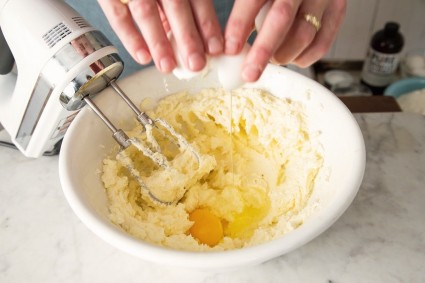 Beating a single egg into a bowl of thick cake batter using an electric hand mixer.