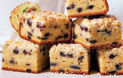 Squares of Sweet Corn and Blueberry Coffee Cake piled on a table, showing a compressed layer of unrisen batter along the bottom.