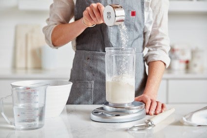 Baker feeding sourdough starter with flour