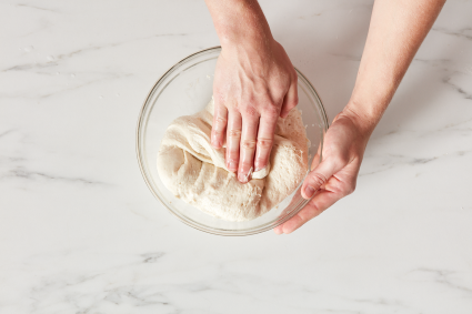 Hands folding a bowl of dough.