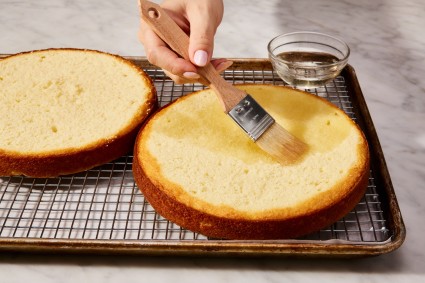 Baker brushing simple syrup cake soak onto round cake layer