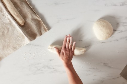 Baker using the heel of one hand to roll tube of baguette dough in the middle