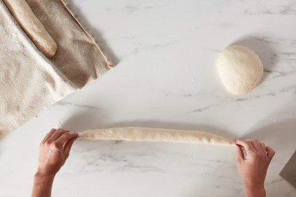 Baker tapering ends of shaped baguette dough