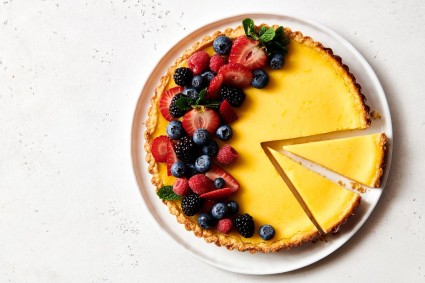 Lemon tart from above with a few slices cut and fresh berries on one side.